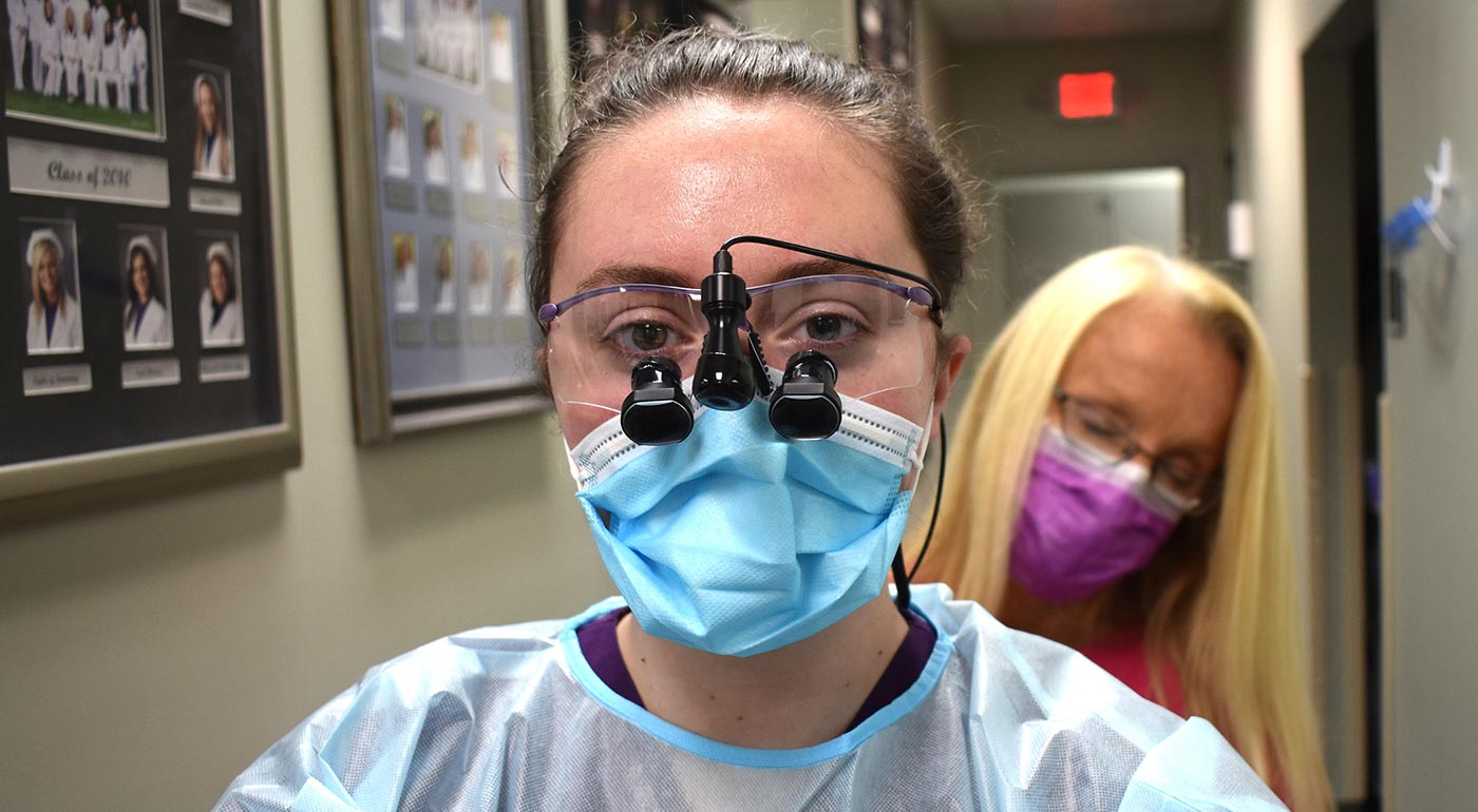 Dental hygiene program director Melinda Gill helps Roane State student Natasha McNeil into the mandatory garb she wears while working with patients. Still to be put on: a hair covering and a face shield.