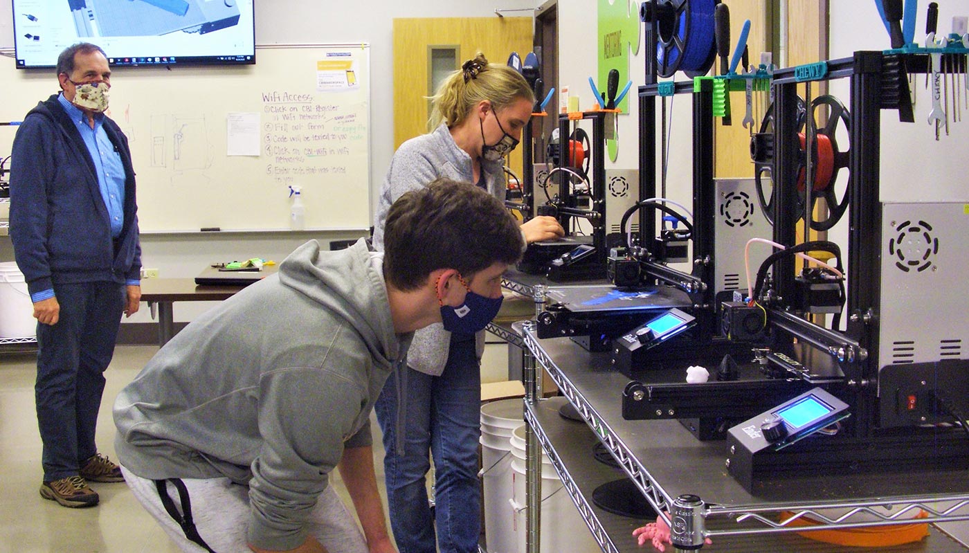 Tom McDunn watches as Roane State students Josh Palmer and Janel Hostetler use 3D printers.
