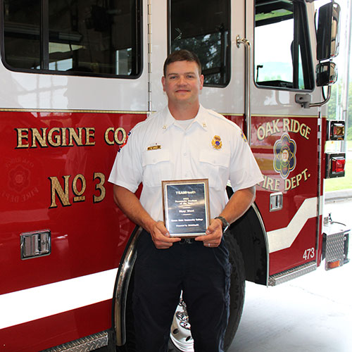 ORFD Captain Shay West hold his Paramedic Student of the Year Award in front of an Oak Ridge fire engine.