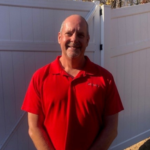 A man in a red shirt standing in front of a fence.