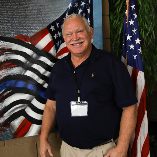 A man standing in front of an American flag background.