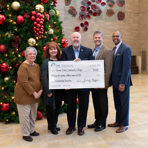 A group of people holding a large check, standing in front of a Christmas tree.