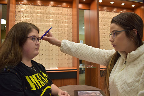 A student helping a patient with eyeglasses.