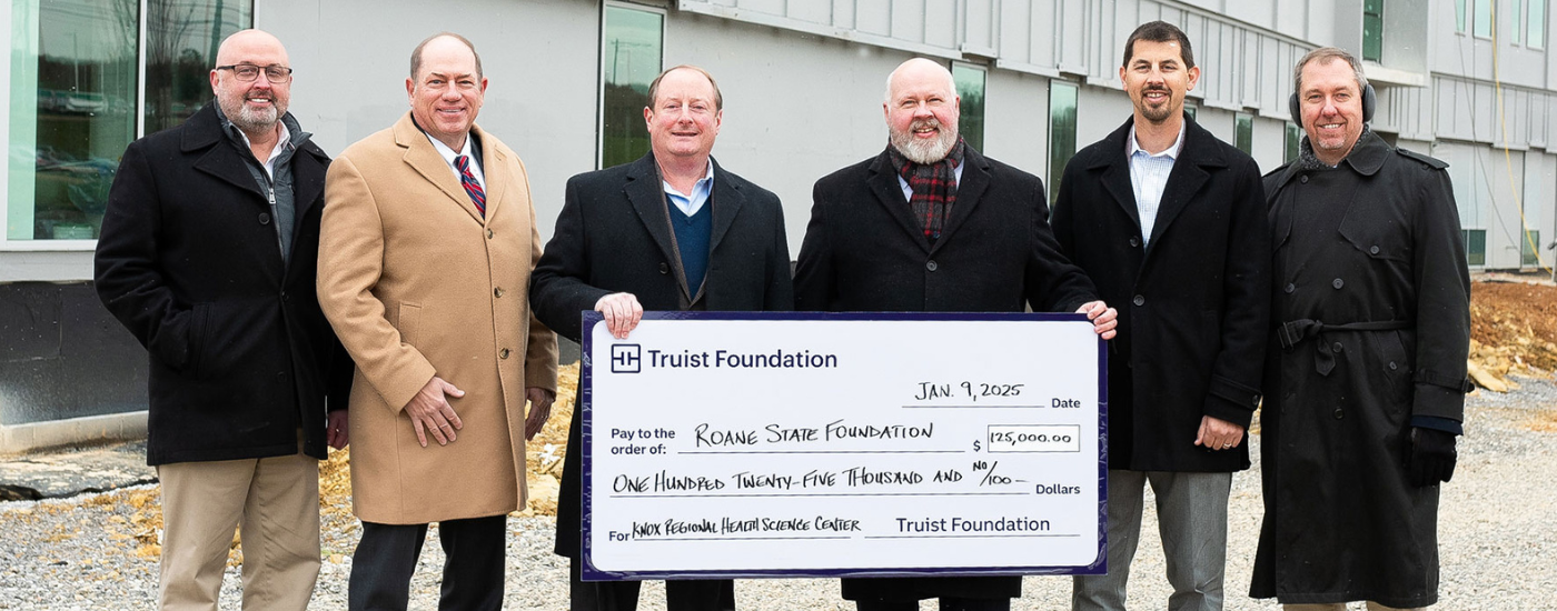 A group of people standing at a construction site holding a check.