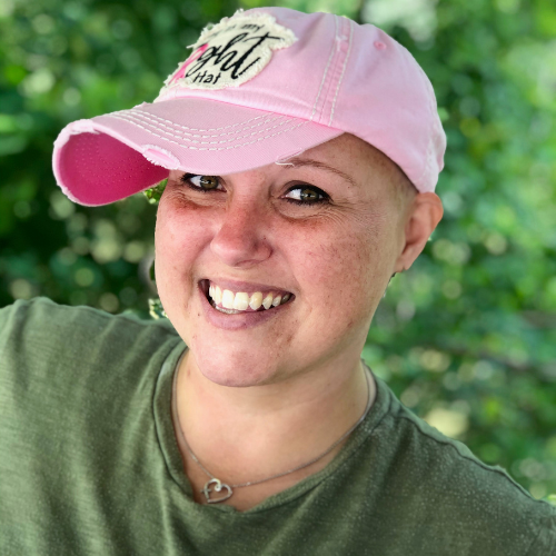 A woman smiling at the camera, wearing a pink breast cancer survivor hat.