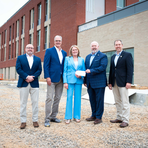 Five people standing in front of a college campus construction site.