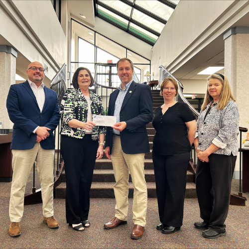 A group of people standing inside a bank lobby holding a check.