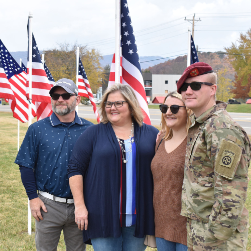A group of people standing in front of American flags; one is in a military uniform.
