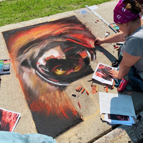 An artist uses chalk to create a design on a sidewalk square.