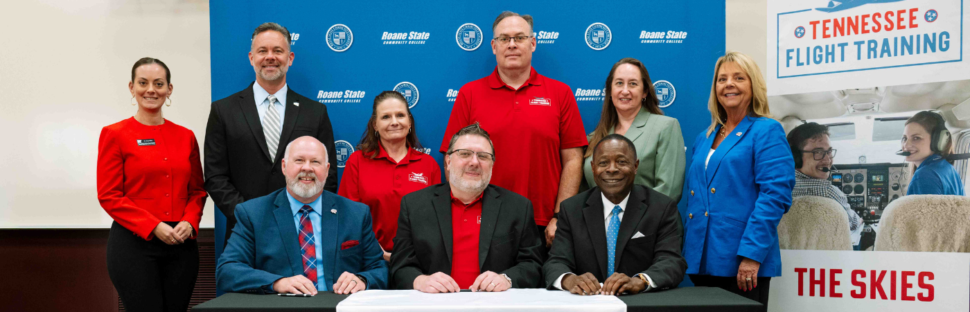 A group of people pose for a photo with Roane State and Tennessee Flight Training signage.