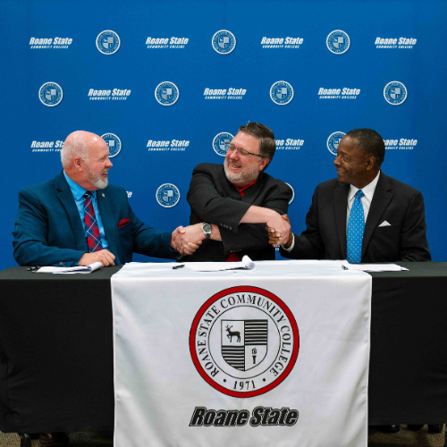 Three people shaking hands while seated at a table.