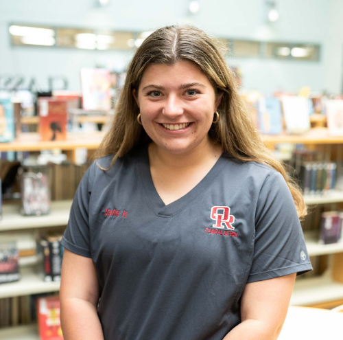 A student in scrubs standing in a library.