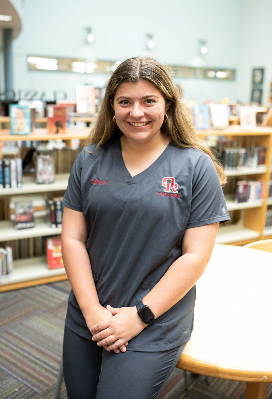 A student in scrubs standing in a library.