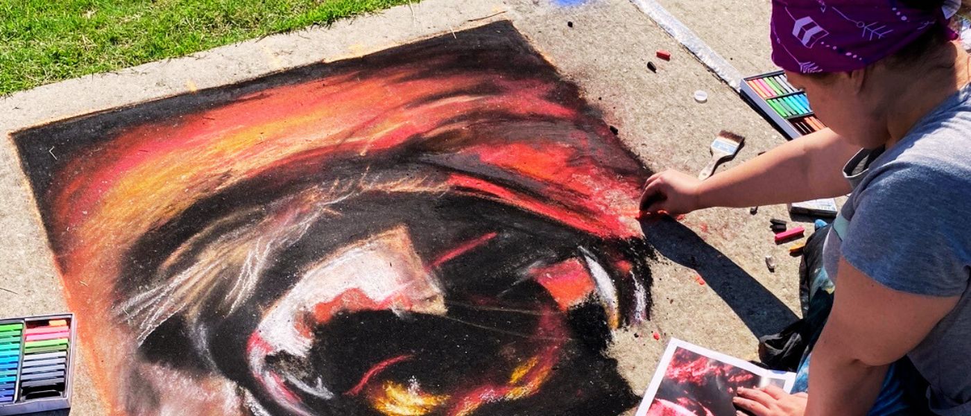 An artist works on their chalk art design on the sidewalk during a previous festival.